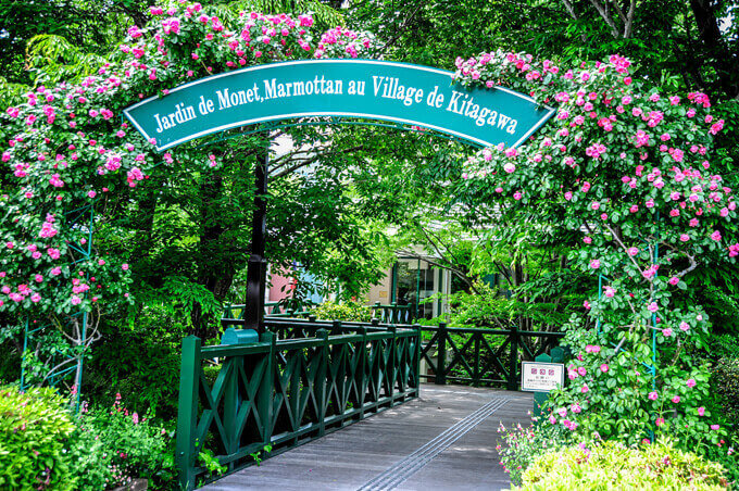 写真：グリーンの看板がついたアーチにたくさんバラが咲いています